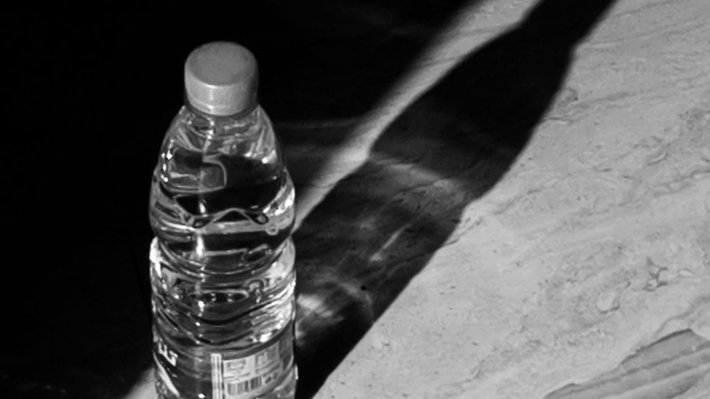 Water bottle on the ground in hard light, a person's shadow falling across it