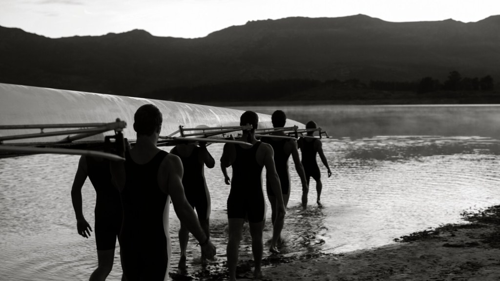 A rowing crew carrying their shell into the water together at dawn